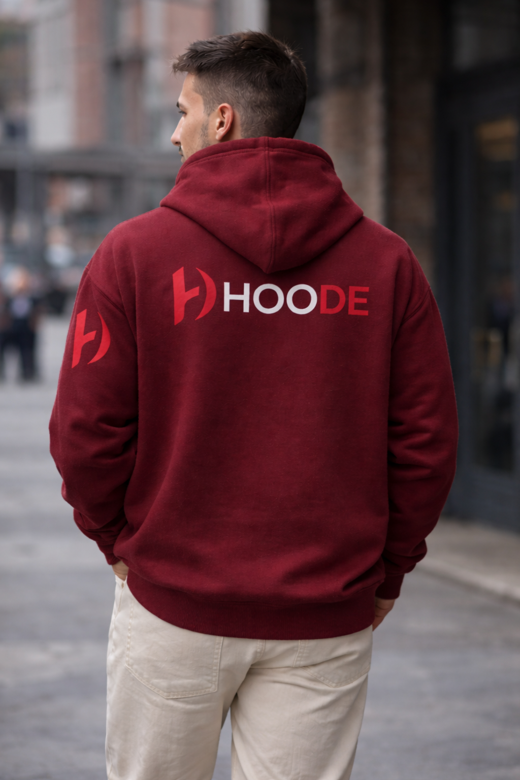 Person wearing a maroon hoodie with 'HOODE' branding on the back, standing in an urban setting.